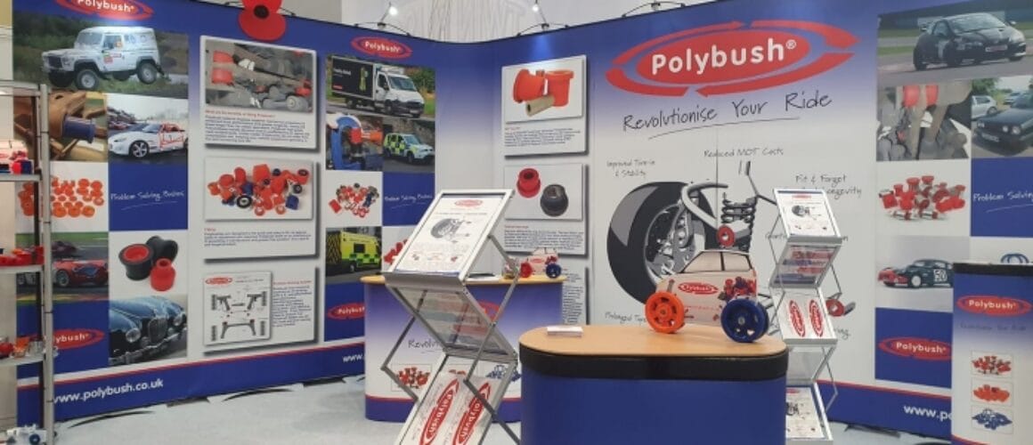 A exhibition stand for polybush featuring displays with car parts, informational panels, and promotional materials. A lectern in the front displays various auto components.