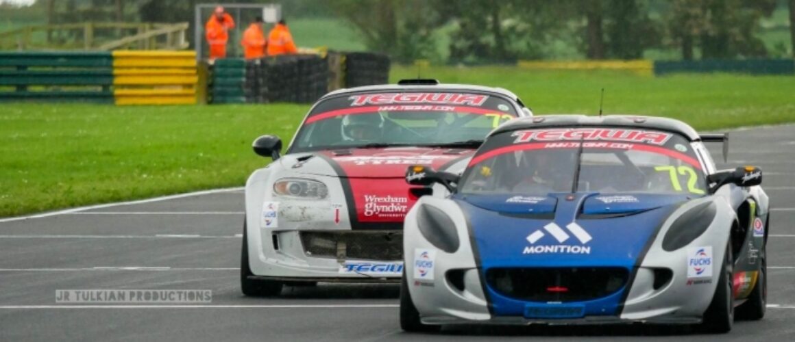 Two racing cars, a white one labelled "1" and a blue one labelled "72," speed on a wet circuit with track marshals visible in the background.