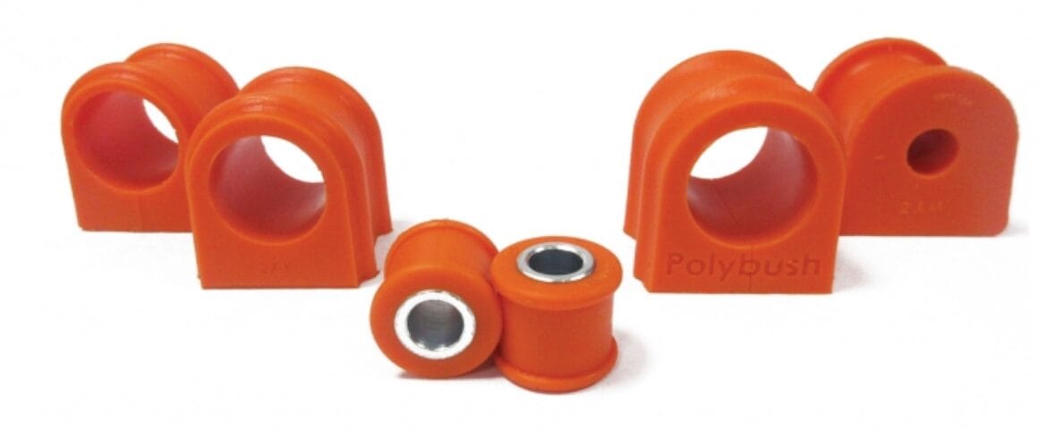 A set of orange polybush brand car suspension bushings, including two larger d-shaped and two smaller cylindrical pieces with metal inlays, displayed against a white backdrop.