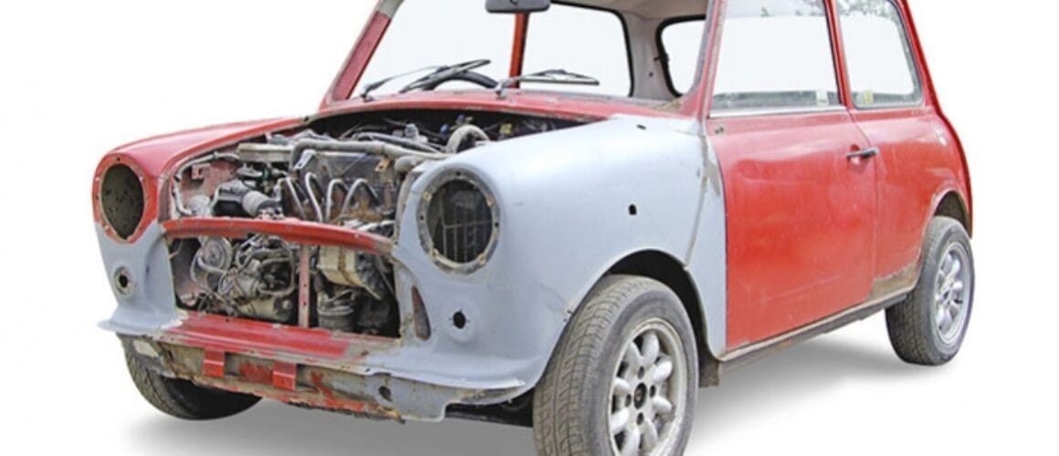 An old, partially dismantled mini car with exposed engine and missing front parts, painted in faded red and white, isolated on a white background.