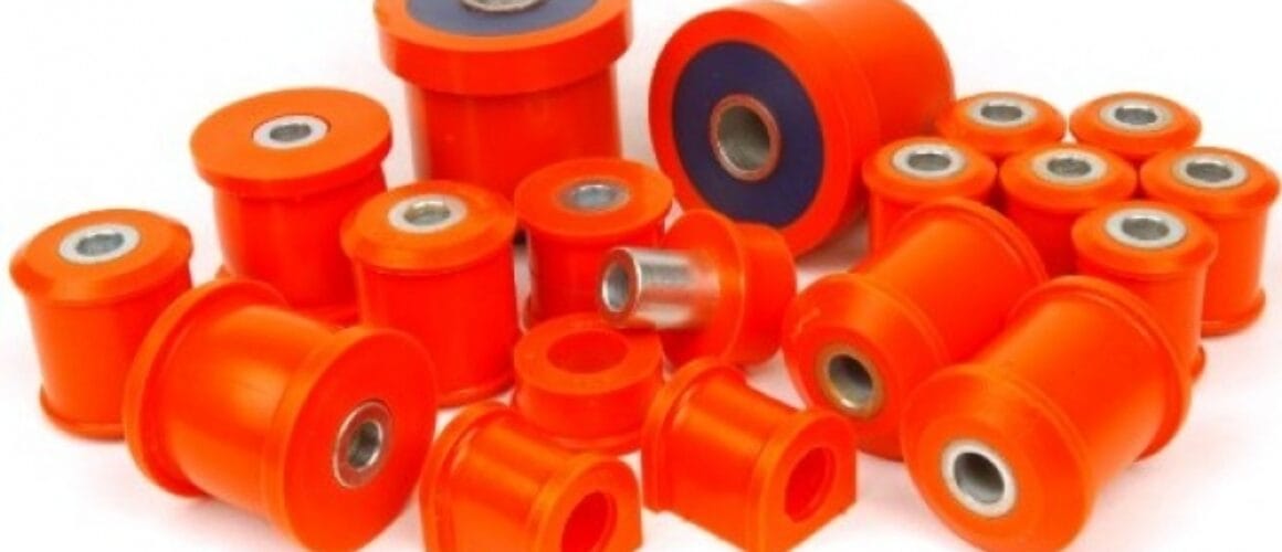 An assortment of orange polyurethane bushes of various sizes, some with metal sleeves, scattered on a white background.