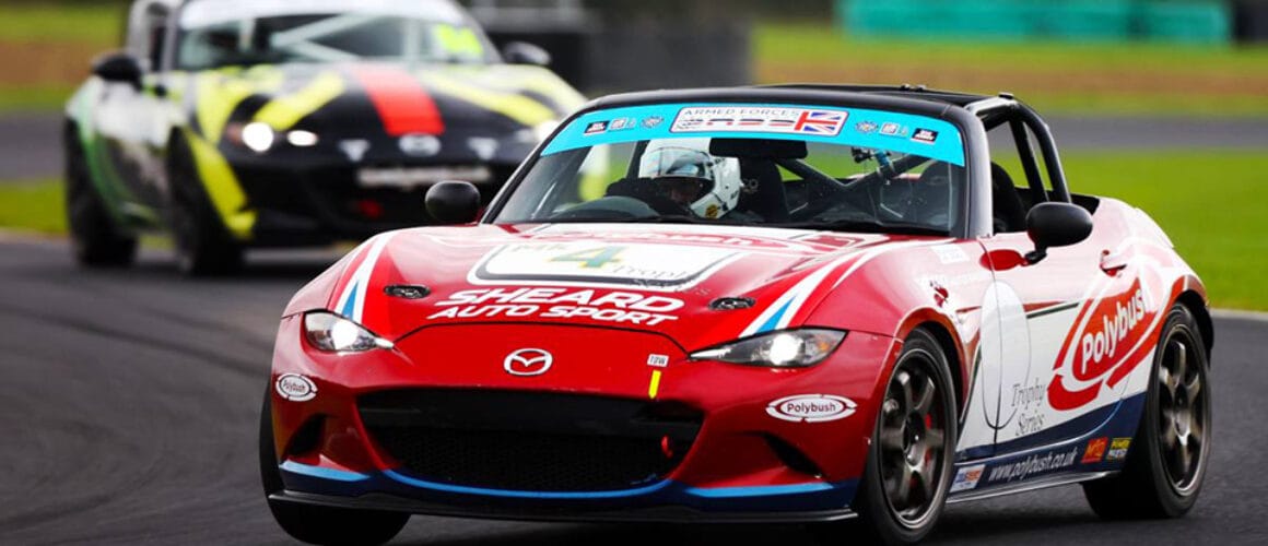 A red racing car with sponsor logos leads another car on a tarmac racetrack, showcasing dynamic motion and competitive racing.