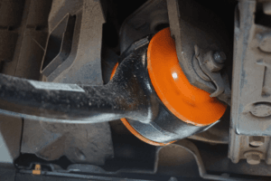 Close-up of an orange shock absorber in the suspension system of a vehicle, showing detailed elements like dust on the components and surrounding metallic parts.