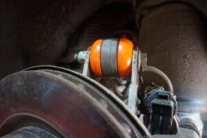 Close-up of a car's suspension featuring an orange shock absorber, with brake disc and other mechanical components visible in the background.