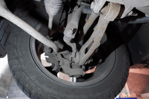 Close-up view of a vehicle's underbody showing suspension components, steering linkage, and a tyre, highlighting the mechanical complexity.