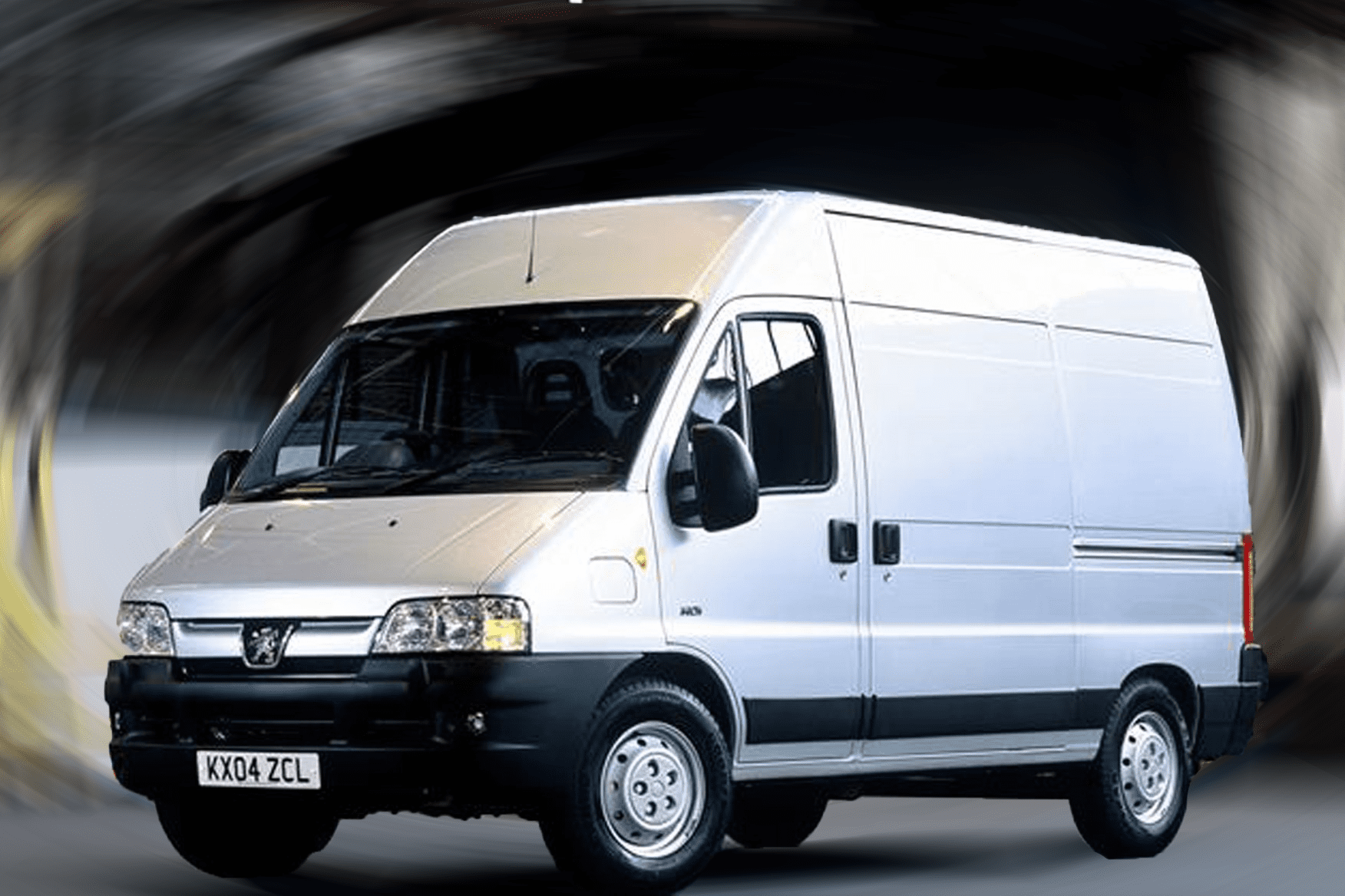 A white cargo van with a blurred background, showcasing the vehicle's front and side view. The van is stationary and displays the registration plate 'kx04 zcl'.