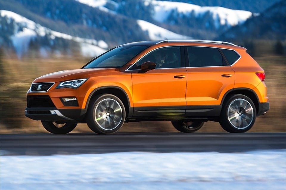 A bright orange 4x4 speeding along a blurred motorway with a snowy mountainous landscape in the background during dusk.