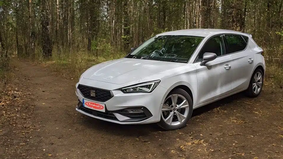 A silver Seat Leon parked on a dirt track surrounded by a dense woodland, showcasing its sleek design and contemporary style.
