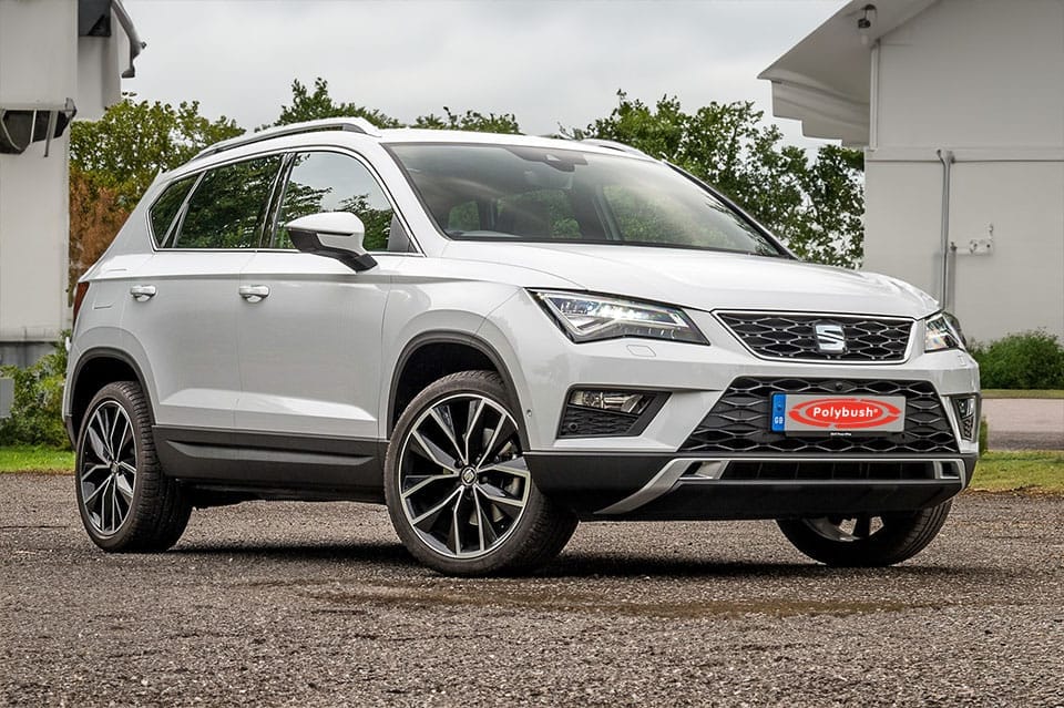 A white Seat Ateca SUV parked on a grey pavement, featuring sleek black trim and large alloy wheels, set against a backdrop of green trees and a cloudy sky. 

(Note: There is no need for translation in this text as, in this case, the same terms are used in both American and British English.)