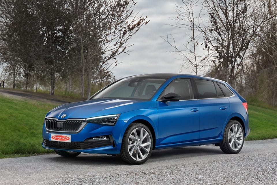 A bright blue Skoda saloon parked on a roadside with leafy trees and grass in the background under a cloudy sky. The car features sleek body lines and contemporary design with silver alloys.