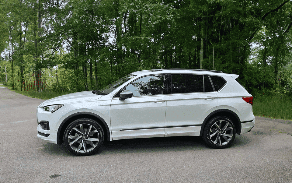 A white 4x4 parked on the side of a road with lush green trees in the background under a clear sky.