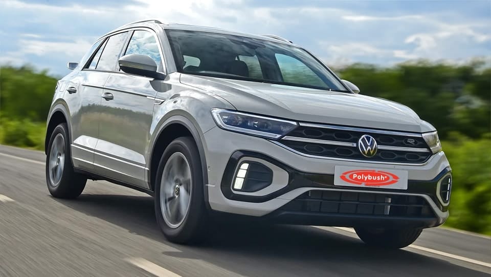 A silver Volkswagen T-Cross SUV driving on a motorway, featuring prominent branding for Polybush on the front. The background shows a blurred green landscape under a cloudy sky.