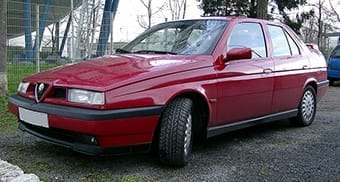 A red Alfa Romeo 164 saloon parked outside, featuring a distinctive v-shaped front grille and sleek body design.