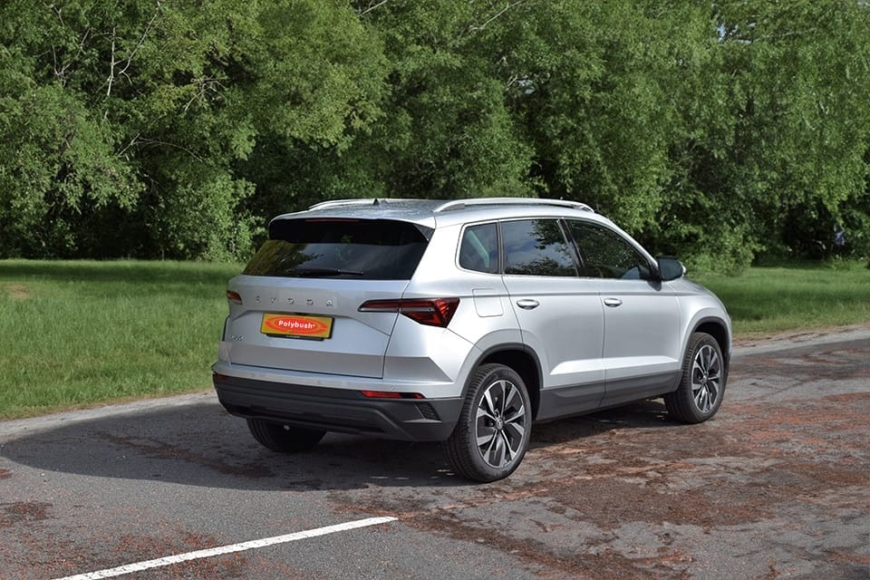 A silver 4x4 parked on a tarmac area beside lush green trees, displayed under a clear day. The car features modern design elements with stylish rear tail lights.