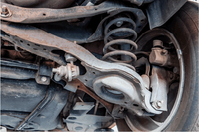 Close-up of a car's underside showing detailed view of suspension system, rusty metal parts, and the wheel assembly.