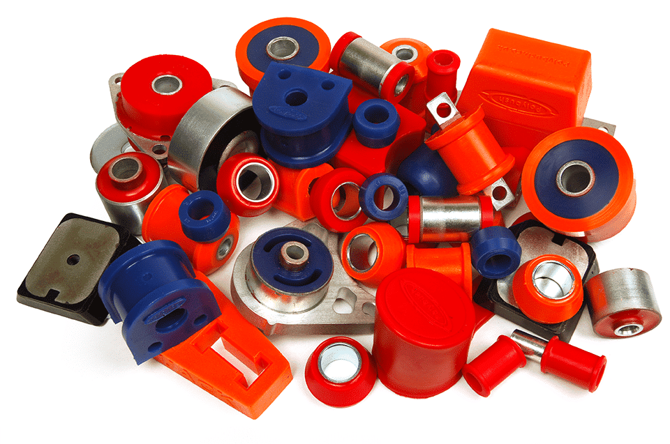 A collection of colourful polyurethane suspension bushings and metal parts, primarily in red, blue, and orange, scattered on a white background.