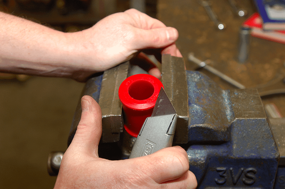 Two hands using a file to shape a red plastic object secured in a metal vice on a workbench, amidst various tools.