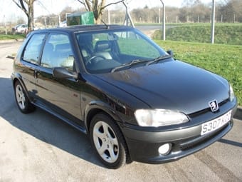 A black Peugeot 306 parked outside on a sunny day, showcasing clean lines and well-kept bodywork, with trees and a fence in the backdrop.