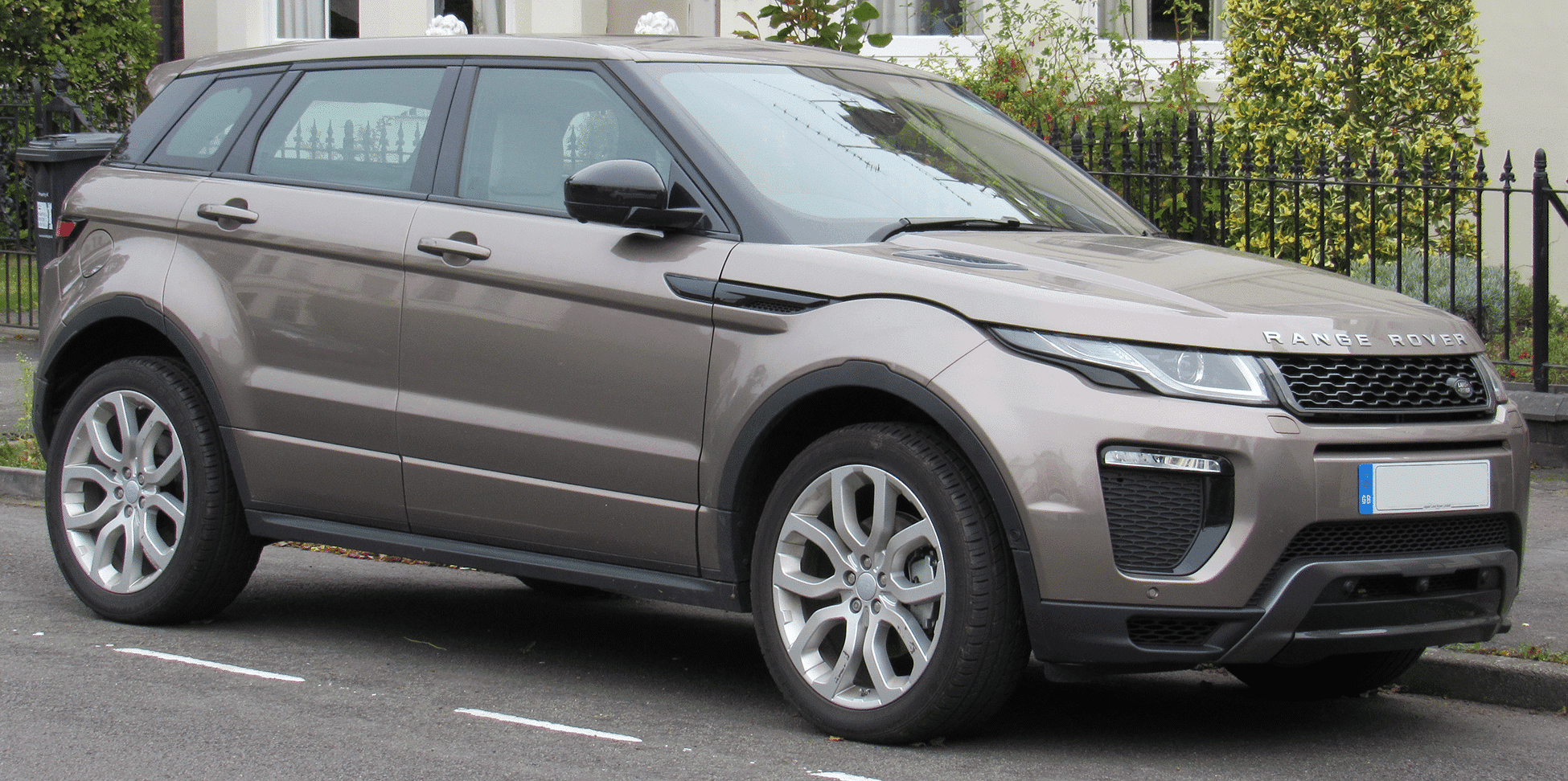 A modern grey range rover suv parked on a suburban street, angled towards the viewer, with residences and greenery in the background.