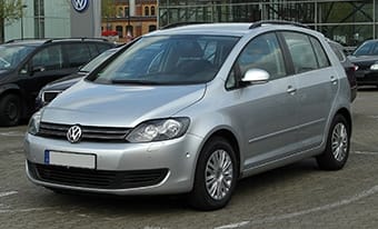 A silver Volkswagen Golf parked in a car park, with other cars and a building in the background. The car is facing slightly to the left with a clean and contemporary design.