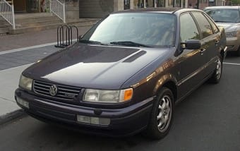 A dark blue volkswagen jetta parked on a city road, featuring clean lines and classic 1990s design, with clear skies in the background.